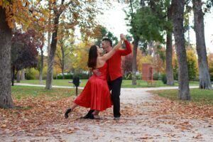 Una pareja baila con gracia en un parque adornado con hojas otoñales, con trajes rojos a juego. Sus movimientos capturan la esencia de las Clases de Bailes de Salón en Madrid, como si vinieran directamente de un vibrante ambiente de la ciudad. - ForTwo - Planes para parejas