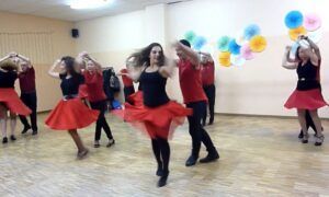 En una animada escena de Clases de Bailes de Salón en Madrid, las parejas bailan con gracia en parejas, sus trajes rojos y negros contrastan con las coloridas decoraciones de las paredes, creando una energía vibrante que captura la esencia del baile en Madrid. - ForTwo - Planes para parejas