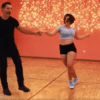 Un hombre y una mujer bailan con gracia en una habitación con paredes naranjas y luces de colores, evocando el encanto de las clases de baile de salón en Madrid. - ForTwo - Planes para parejas