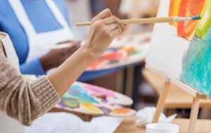 Primer plano de alguien que asiste a Clases de Dibujo y Pintura en Zaragoza, pintando sobre un lienzo con un pincel y sosteniendo una paleta llena de colores vibrantes. - ForTwo - Planes para parejas