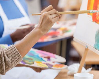 Primer plano de alguien que asiste a Clases de Dibujo y Pintura en Zaragoza, pintando sobre un lienzo con un pincel y sosteniendo una paleta llena de colores vibrantes. - ForTwo - Planes para parejas