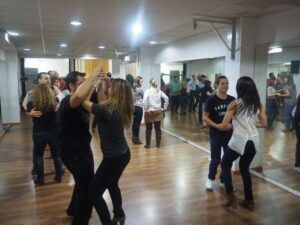 Las parejas se mueven con gracia en un estudio de baile con espejos y suelos de madera, inmersas en el vibrante ritmo de la salsa cubana, perfeccionando sus movimientos durante emocionantes clases de salsa cubana en Madrid. - ForTwo - Planes para parejas