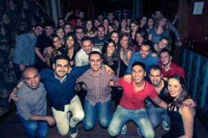 Una multitud animada se reunió en una sala poco iluminada de Madrid, sonriendo y posando para una foto después de disfrutar de Clases de Salsa Cubana en Madrid. - ForTwo - Planes para parejas
