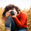 Un individuo de pelo rizado con una camisa naranja captura un retrato fotográfico en un campo de trigo dorado, posiblemente aplicando habilidades del Curso de Retrato Fotográfico en Zaragoza. - ForTwo - Planes para parejas