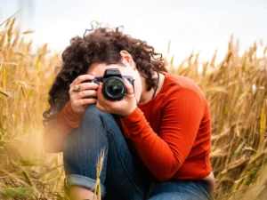 Un individuo de pelo rizado con una camisa naranja captura un retrato fotográfico en un campo de trigo dorado, posiblemente aplicando habilidades del Curso de Retrato Fotográfico en Zaragoza. - ForTwo - Planes para parejas