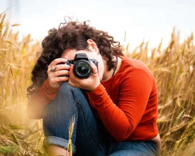 Un individuo de pelo rizado con una camisa naranja captura un retrato fotográfico en un campo de trigo dorado, posiblemente aplicando habilidades del Curso de Retrato Fotográfico en Zaragoza. - ForTwo - Planes para parejas