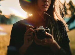 En Zaragoza, una persona utiliza una cámara Pentax al aire libre, con la luz del sol y un sombrero proyectando sombras artísticas en su rostro, perfeccionando las habilidades del Curso de Retrato Fotográfico en Zaragoza. - ForTwo - Planes para parejas