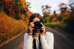 Fotógrafo con cámara en un camino rural entre vibrantes árboles otoñales, encarnando el espíritu del "Curso de Retrato Fotográfico en Zaragoza". - ForTwo - Planes para parejas