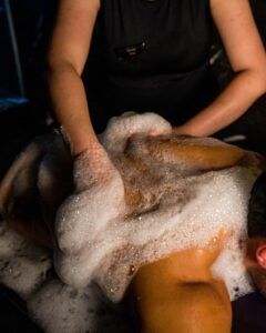 En un entorno con poca luz en Madrid, la mitad de una pareja disfruta de un relajante masaje con espuma y jabón, que evoca la Experiencia Las Mil y Una Noches para parejas en Madrid. - ForTwo - Planes para parejas