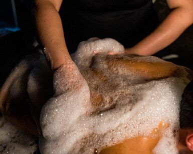 En un entorno con poca luz en Madrid, la mitad de una pareja disfruta de un relajante masaje con espuma y jabón, que evoca la Experiencia Las Mil y Una Noches para parejas en Madrid. - ForTwo - Planes para parejas