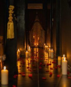 El pasillo tenuemente iluminado de Madrid, adornado con velas y pétalos de rosas rojas, evoca la magia de la Experiencia Las Mil y Una Noches para parejas, guiándote a una entrada cubierta con cortinas para una experiencia inolvidable. - ForTwo - Planes para parejas