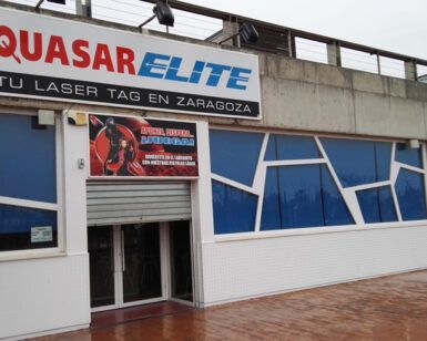 El Laser Tag en Zaragoza con Quasar Elite presenta un exterior deslumbrante con diseños geométricos de ventanas que se reflejan en el suelo mojado, invitando a los amantes de las emociones fuertes a una aventura de laser tag inolvidable. - ForTwo - Planes para parejas