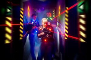 Tres personas disfrutan de una emocionante sesión de Lasertag en las salas tenuemente iluminadas de Laserspace Zaragoza, vistiendo chalecos iluminados y apuntando con pistolas láser como parte de la emocionante experiencia Pack Ocio. - ForTwo - Planes para parejas