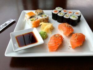 Una selección de piezas de sushi con salsa de soja, wasabi y jengibre en un plato cuadrado blanco personifica el arte que se enseña en "Taller de Cocina Japonesa: Aprende a Preparar Sushi, Gyozas y Más. - ForTwo - Planes para parejas