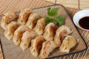 Un plato de gyozas asadas con guarnición, similar a la auténtica cocina japonesa, combinado con un plato pequeño de salsa de soja, inspirado en "Taller de Cocina Japonesa: Aprende a Preparar Sushi, Gyozas y Más. - ForTwo - Planes para parejas