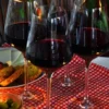 Cuatro copas de vino tinto Premium Vinos Brabantino: Cata Privada de Sabores descansan sobre un mantel a cuadros rojos junto a un plato de aperitivos y una vela encendida, creando un ambiente íntimo. - ForTwo - Planes para parejas