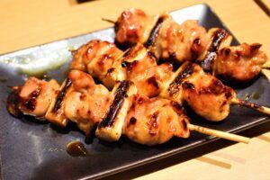 Brochetas de pollo a la parrilla con glaseado, servidas con delicadas gyozas en un elegante plato negro, del "Taller de Cocina Japonesa: Aprende a Preparar Sushi, Gyozas y Más. - ForTwo - Planes para parejas