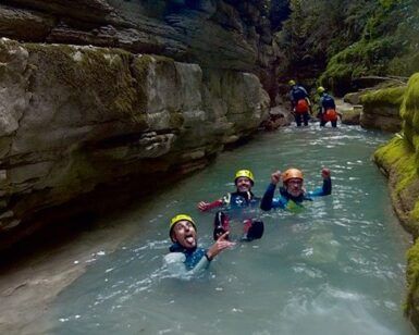 Tres buscadores de emociones con cascos caminan alegremente por un arroyo rocoso, disfrutando del Barranquismo en Huesca para Principiantes con Anayet Aventura en medio de los impresionantes paisajes de Huesca. - ForTwo - Planes para parejas