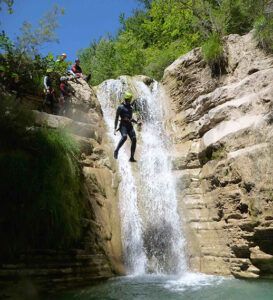 Una persona que desciende por una cascada en Huesca, con la mirada puesta en las rocas, disfruta de la exuberante vegetación. Esta emocionante experiencia, guiada por Barranquismo en Huesca para Principiantes con Anayet Aventura, captura la emoción del barranquismo en un vibrante entorno natural. - ForTwo - Planes para parejas