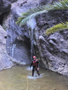 Una persona en Barranquismo en Los Carrizales, Tenerife: El equipo de Aventura Extrema se encuentra debajo de una cascada en el estrecho y rocoso cañón de Los Carrizales, con hojas de palmera meciéndose suavemente arriba. - ForTwo - Planes para parejas