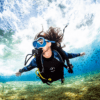 Durante su Bautismo de Buceo en El Hierro: Vive tu Primera Inmersión, un buzo nada bajo el agua cerca de un banco de peces, mientras la luz del sol se filtra a través del agua frente a la costa de El Hierro. - ForTwo - Planes para parejas
