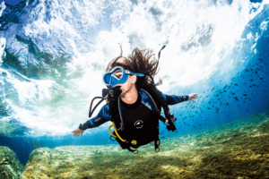 Durante su Bautismo de Buceo en El Hierro: Vive tu Primera Inmersión, un buzo nada bajo el agua cerca de un banco de peces, mientras la luz del sol se filtra a través del agua frente a la costa de El Hierro. - ForTwo - Planes para parejas