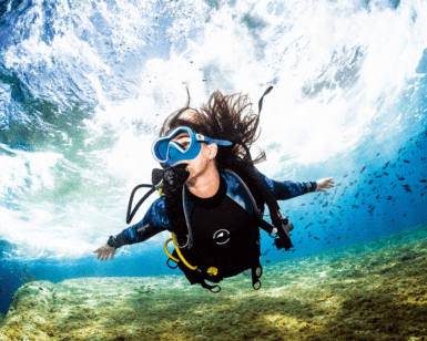 Durante su Bautismo de Buceo en El Hierro: Vive tu Primera Inmersión, un buzo nada bajo el agua cerca de un banco de peces, mientras la luz del sol se filtra a través del agua frente a la costa de El Hierro. - ForTwo - Planes para parejas