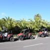 Cuatro vehículos de Buggy Tour en La Palma están estacionados en una carretera iluminada por el sol bordeada de palmeras ondulantes, bajo un cielo azul claro, listos para una aventura inolvidable. - ForTwo - Planes para parejas