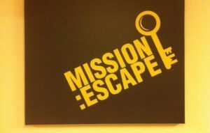 Un gráfico clave y el texto amarillo "MISIÓN: ESCAPE" sobre un fondo negro capturan la emoción de una aventura de Room Escape, inspirada en Cara Oculta - Room Escape. - ForTwo - Planes para parejas