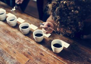 Una persona participa en la Cata Sensorial de Café, probando ricos sabores y fragancias de múltiples tazas en una mesa de madera, usando una cuchara para saborear cada nota. - ForTwo - Planes para parejas