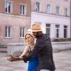 Una pareja baila elegantemente al aire libre, con la mujer con un vestido azul y el hombre con sombrero y camisa negra, capturando la esencia de Clases de Baile Latino en Monzón: Salsa Cubana contra vibrantes edificios de color rosa. - ForTwo - Planes para parejas