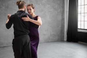Una pareja baila Salsa elegantemente en una espaciosa sala con grandes ventanales y paredes grises, capturando la esencia de las vibrantes "Clases de Salsa en Huesca: Aprende a Bailar con Ritmo y Pasión". - ForTwo - Planes para parejas