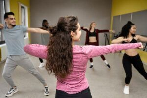 En un animado estudio de paredes grises y amarillas, la gente irradia alegría mientras se estira y se mueve en sus Clases de Salsa en Huesca: Aprende a Bailar con Ritmo y Pasión. - ForTwo - Planes para parejas