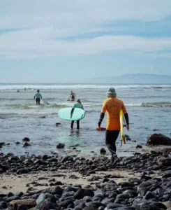 Con trajes de neopreno, las parejas se dirigen a las playas rocosas de Las Américas de Tenerife con sus tablas de surf para "Clases de Surf para parejas", ansiosas por abrazar el océano bajo un cielo nublado. - ForTwo - Planes para parejas