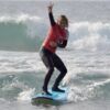 Un surfista con camiseta roja surfea una ola cerca de Tenerife, sonriendo y haciendo el símbolo de la paz. Es el día perfecto para las clases de surf privadas en Volcano Surf School Tenerife. - ForTwo - Planes para parejas