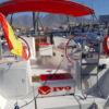 Un impresionante velero con toldo rojo y ruedas de timón dobles está atracado en el vibrante puerto deportivo de Costa Adeje, adornado con una bandera española en la popa, listo para su próximo "Crucero de 3 Horas en Costa Adeje". - ForTwo - Planes para parejas