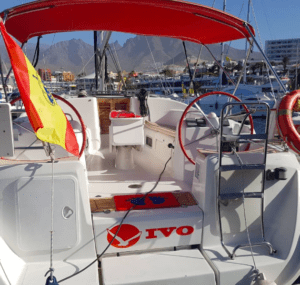 Un impresionante velero con toldo rojo y ruedas de timón dobles está atracado en el vibrante puerto deportivo de Costa Adeje, adornado con una bandera española en la popa, listo para su próximo "Crucero de 3 Horas en Costa Adeje". - ForTwo - Planes para parejas