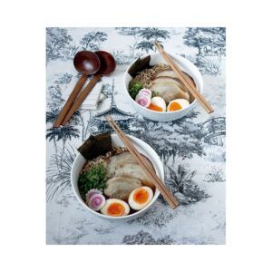 Dos tazones de ramen con huevos, carne y algas descansan sobre una superficie blanca y negra, flanqueados por palillos de madera, creando una fusión de sabores que evocan la experiencia del "Curso: Domina la Olla Rápida y Cocina Sabores del Mundo". - ForTwo - Planes para parejas