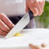 Usando un cuchillo de chef, alguien corta jengibre sobre una superficie de mármol mientras realiza el "Curso de Cocina para Principiantes: Saca al Chef que Llevas Dentro". - ForTwo - Planes para parejas