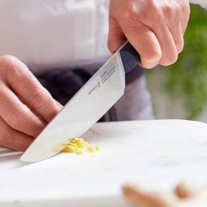 Usando un cuchillo de chef, alguien corta jengibre sobre una superficie de mármol mientras realiza el "Curso de Cocina para Principiantes: Saca al Chef que Llevas Dentro". - ForTwo - Planes para parejas