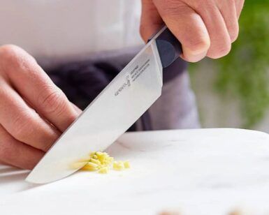 Usando un cuchillo de chef, alguien corta jengibre sobre una superficie de mármol mientras realiza el "Curso de Cocina para Principiantes: Saca al Chef que Llevas Dentro". - ForTwo - Planes para parejas