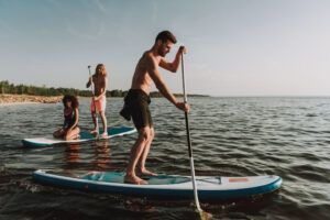 Bajo un cielo azul claro, tres personas disfrutan de un Curso de Iniciación al Stand Up Paddle en Tenerife en aguas tranquilas cerca de la pintoresca costa. - ForTwo - Planes para parejas