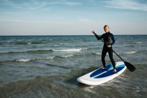 Vestido con un elegante traje de neopreno y sosteniendo un remo, alguien navega con gracia por las tranquilas aguas del océano de Tenerife con el "Curso de Iniciación al Stand Up Paddle en Tenerife". - ForTwo - Planes para parejas