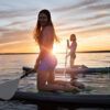 Dos personas arrodilladas sobre tablas de paddle surf al atardecer, sonriendo mientras navegan por las tranquilas aguas durante un Curso de Iniciación al Stand Up Paddle en Tenerife. - ForTwo - Planes para parejas