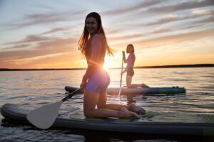 Dos personas arrodilladas sobre tablas de paddle surf al atardecer, sonriendo mientras navegan por las tranquilas aguas durante un Curso de Iniciación al Stand Up Paddle en Tenerife. - ForTwo - Planes para parejas
