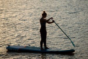Una persona rema con gracia al atardecer en las tranquilas aguas de Tenerife, encarnando la serena belleza que se enseña en el "Curso de Iniciación al Stand Up Paddle en Tenerife". - ForTwo - Planes para parejas