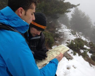 Dos personas con ropa de invierno se encuentran en un sendero nevado y brumoso en Huesca, participando en el Curso de Orientación en Montaña con Mapa y Brújula para una navegación precisa. - ForTwo - Planes para parejas