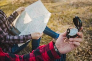 Una persona sostiene una brújula con un mapa sobre la hierba, personificando el Curso de Orientación en Montaña con Mapa y Brújula en Huesca, quizás navegando por los impresionantes paisajes de Huesca. - ForTwo - Planes para parejas