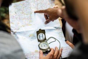 Manos usando un mapa y brújula del "Curso de Orientación en Montaña con Mapa y Brújula en Huesca", con una persona apuntando para navegar por los accidentados terrenos de Huesca. - ForTwo - Planes para parejas