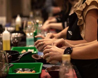 Los participantes, ataviados con delantales, están ocupados preparando comida en el Curso de cocina: Postureo Gastronómico, con ingredientes frescos y utensilios cuidadosamente dispuestos en el mostrador. - ForTwo - Planes para parejas